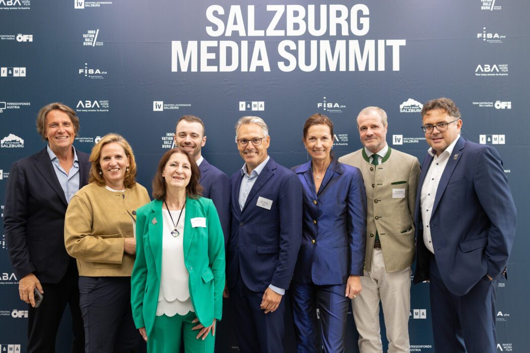 Gruppenfoto mit 8 Personen: die Partner:innen des 20. Salzburg Media Summits vor einer Fotowand mit Logos