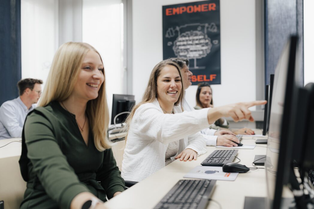 Mitarbeiter:innen von COPA-DATA, eine Frau zeigt einer anderen Frau etwas auf einem Bildschirm, beide lachen