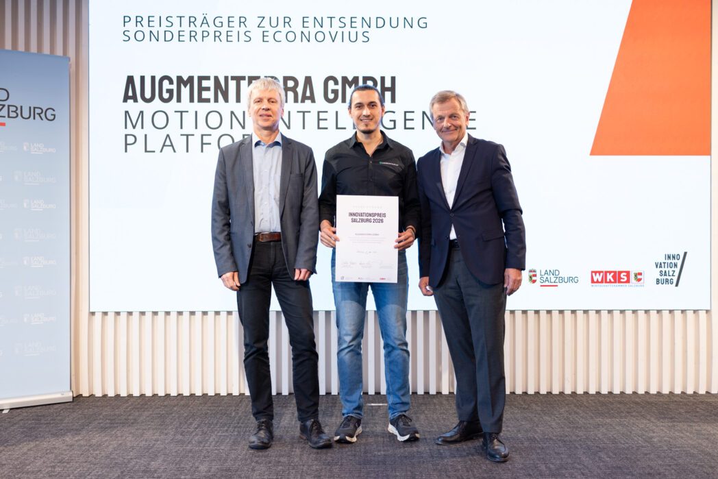Drei Männer auf der Bühne des Salzburger Innovationspreis 2026. Der Mann in der Mitte hält eine Urkunde (AUGMENTERRA) für die Nominierung zum Sonderpreis ECONOVIUS.