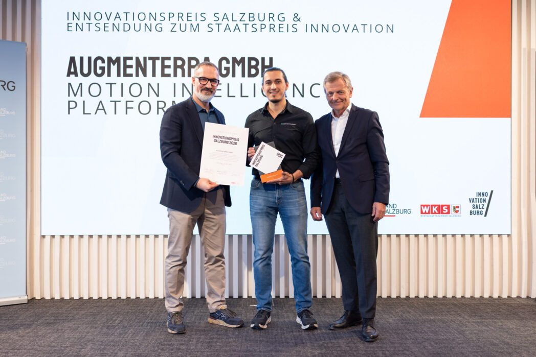 Drei Männer auf der Bühne des Salzburger Innovationspreis 2026. In der Mitte hält ein Mann den Award "Innovationspreis Salzburg 2026" (AUGMENTERRA), links hält ein Mann eine Urkunde.