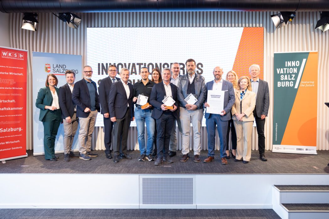Gruppenfoto mit mehreren Personen auf der Bühne des Salzburger Innovationspreis 2026. Drei Personen in der Mitte halten einen Award, eine Person eine Urkunde.