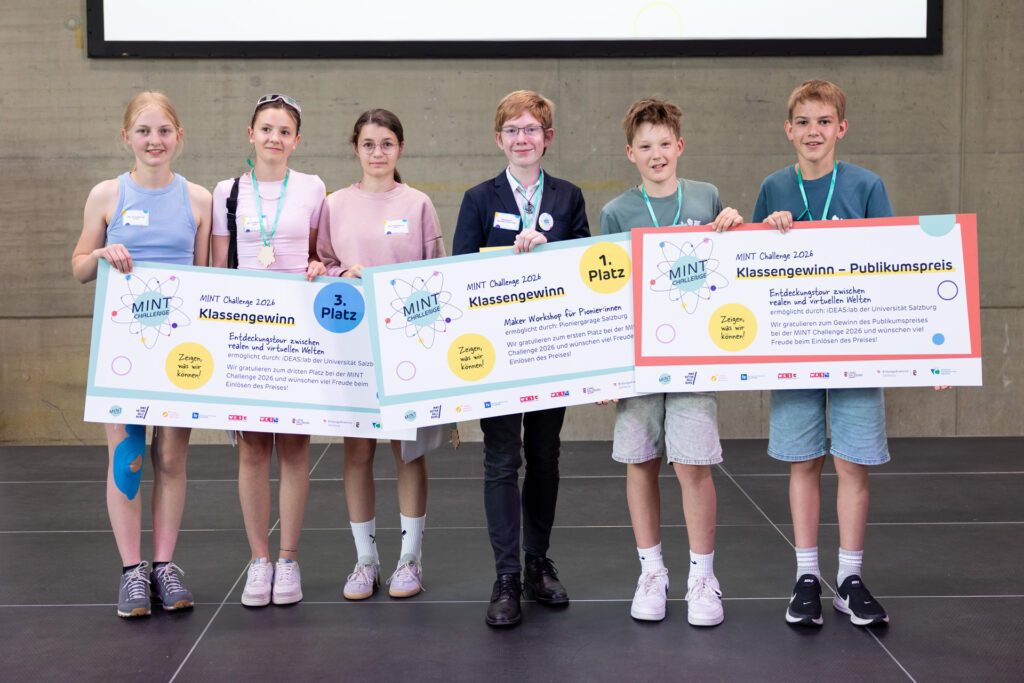 Schülerinnen und Schüler präsentieren ihre Siegerurkunden und Preise bei der MINT Challenge 2026 in Salzburg auf einer Bühne.